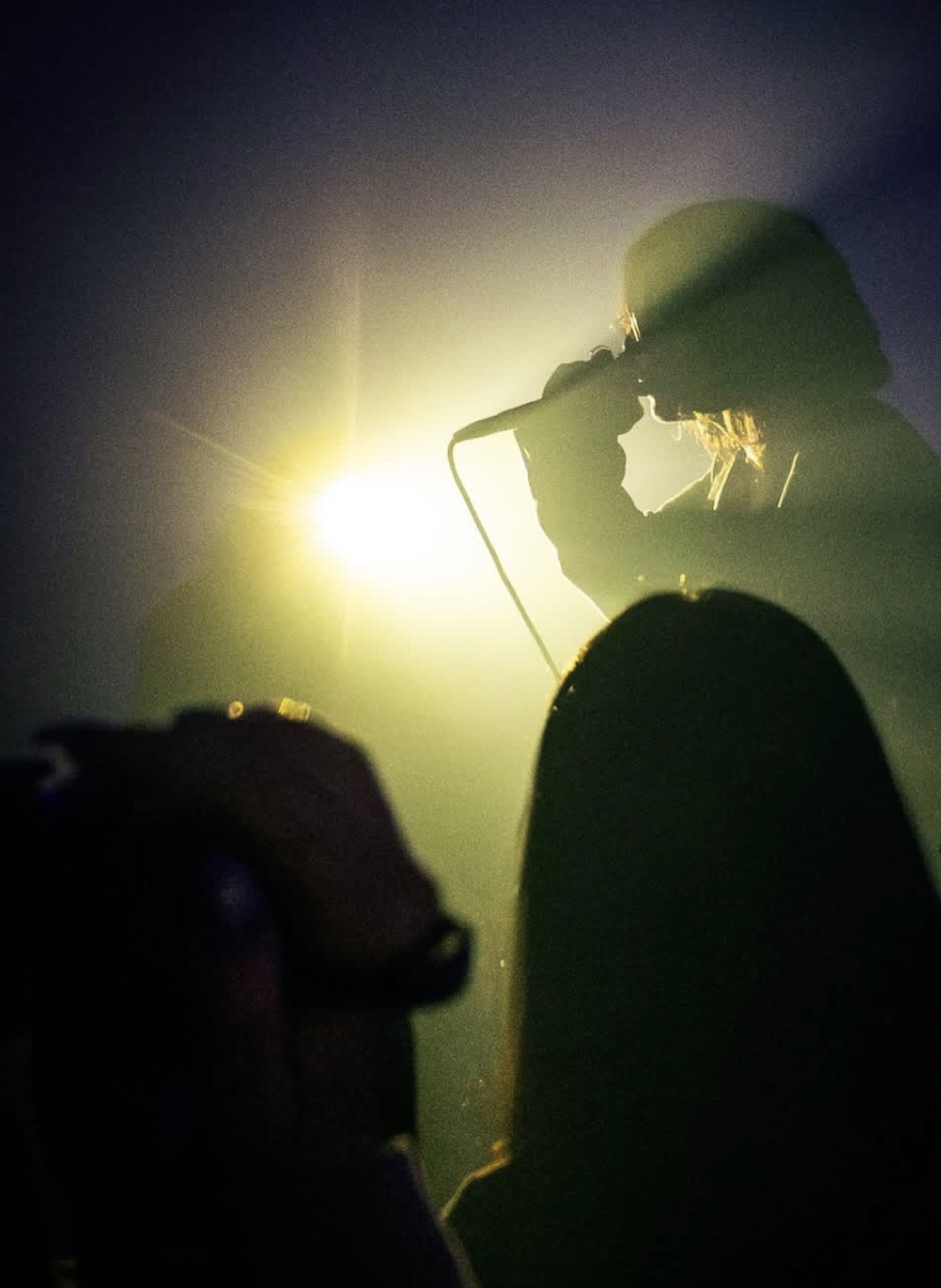 nomu silhouetted at the mic against a stage light flare
